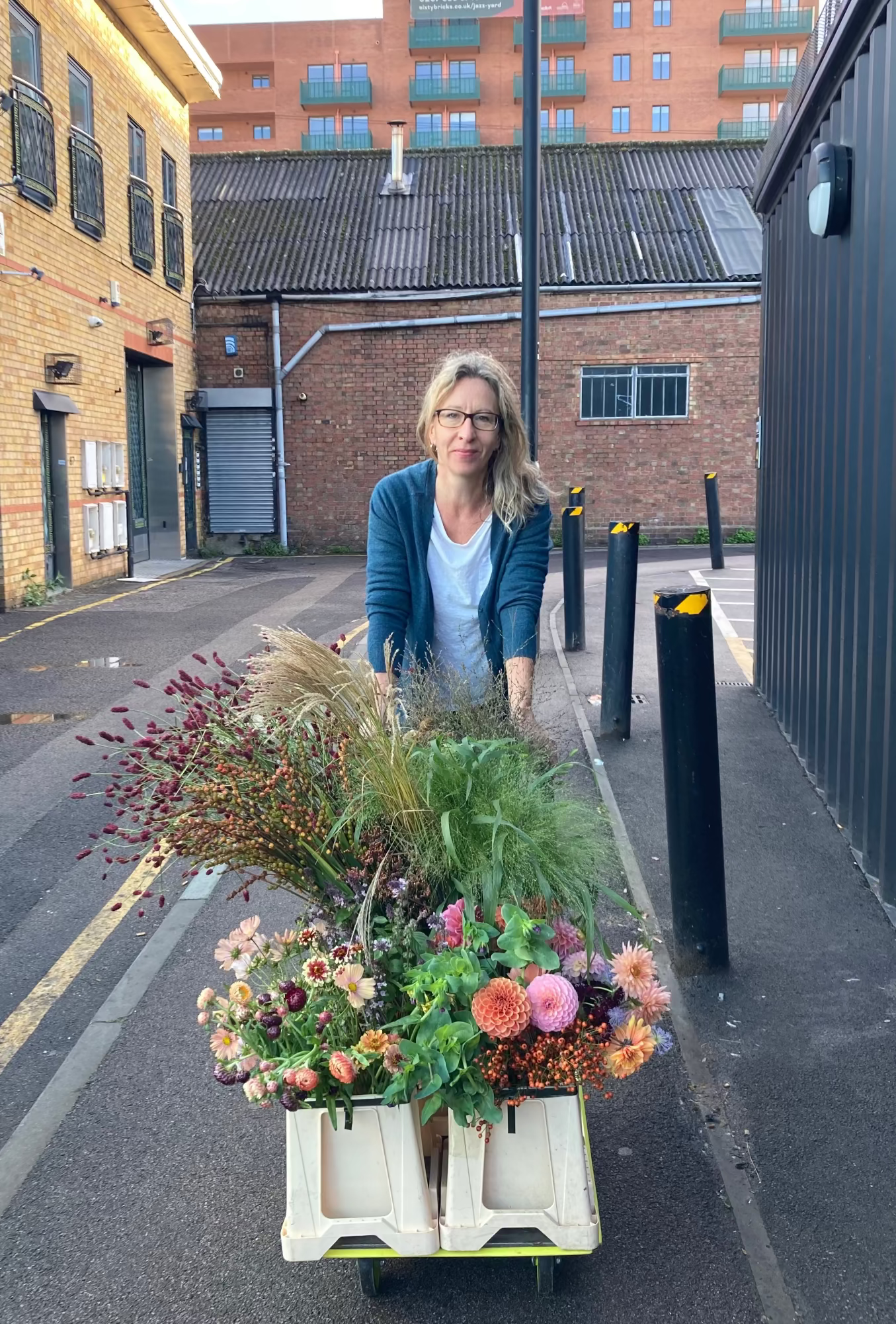 Person pushing a cart with flowers on a street in an urban setting. Flowers are from local flower farm and have wild garden look