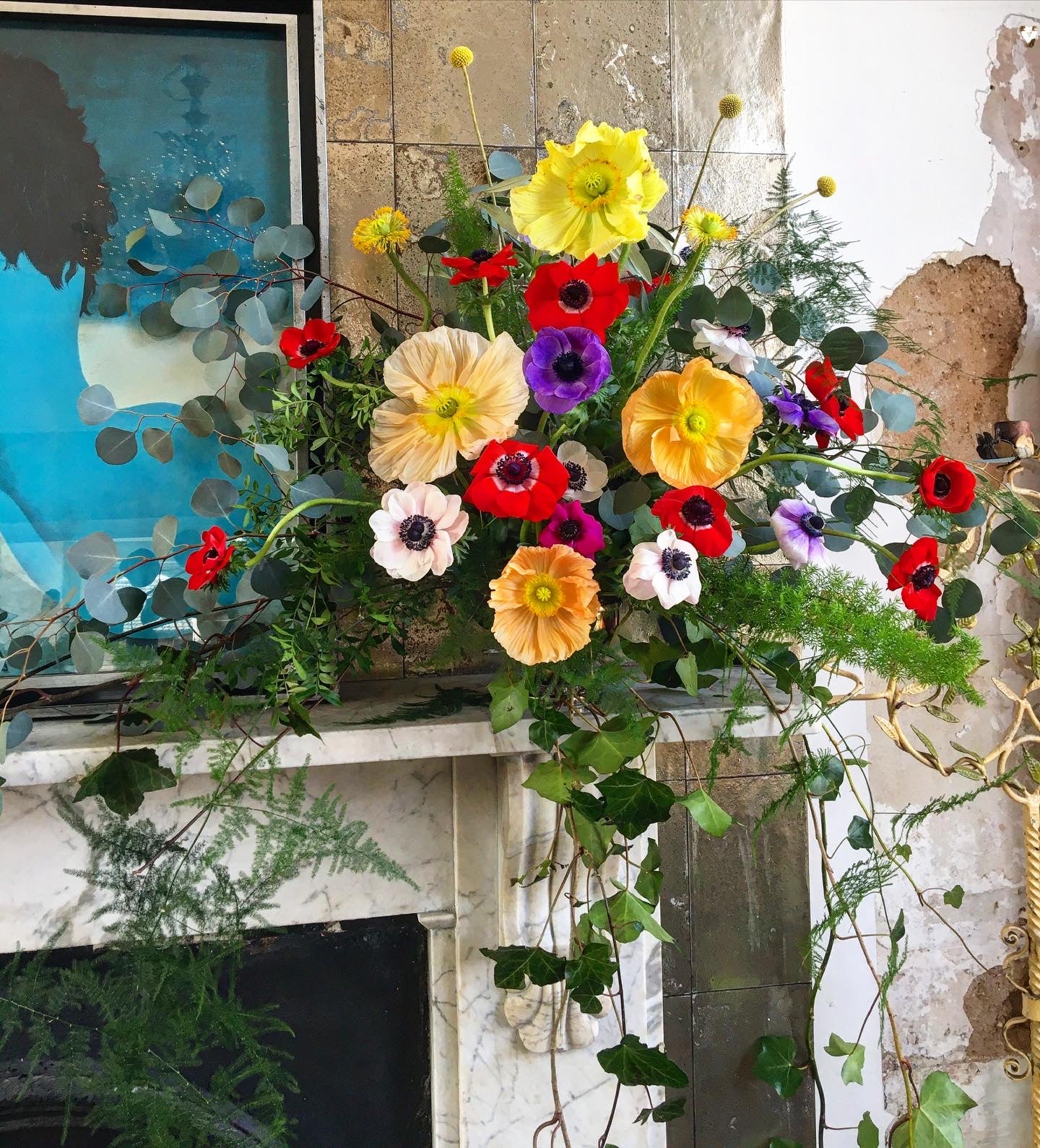 Colourful flower arrangement on a fireplace mantel with a textured wall background. Flowers include anemone and Icelandic poppies