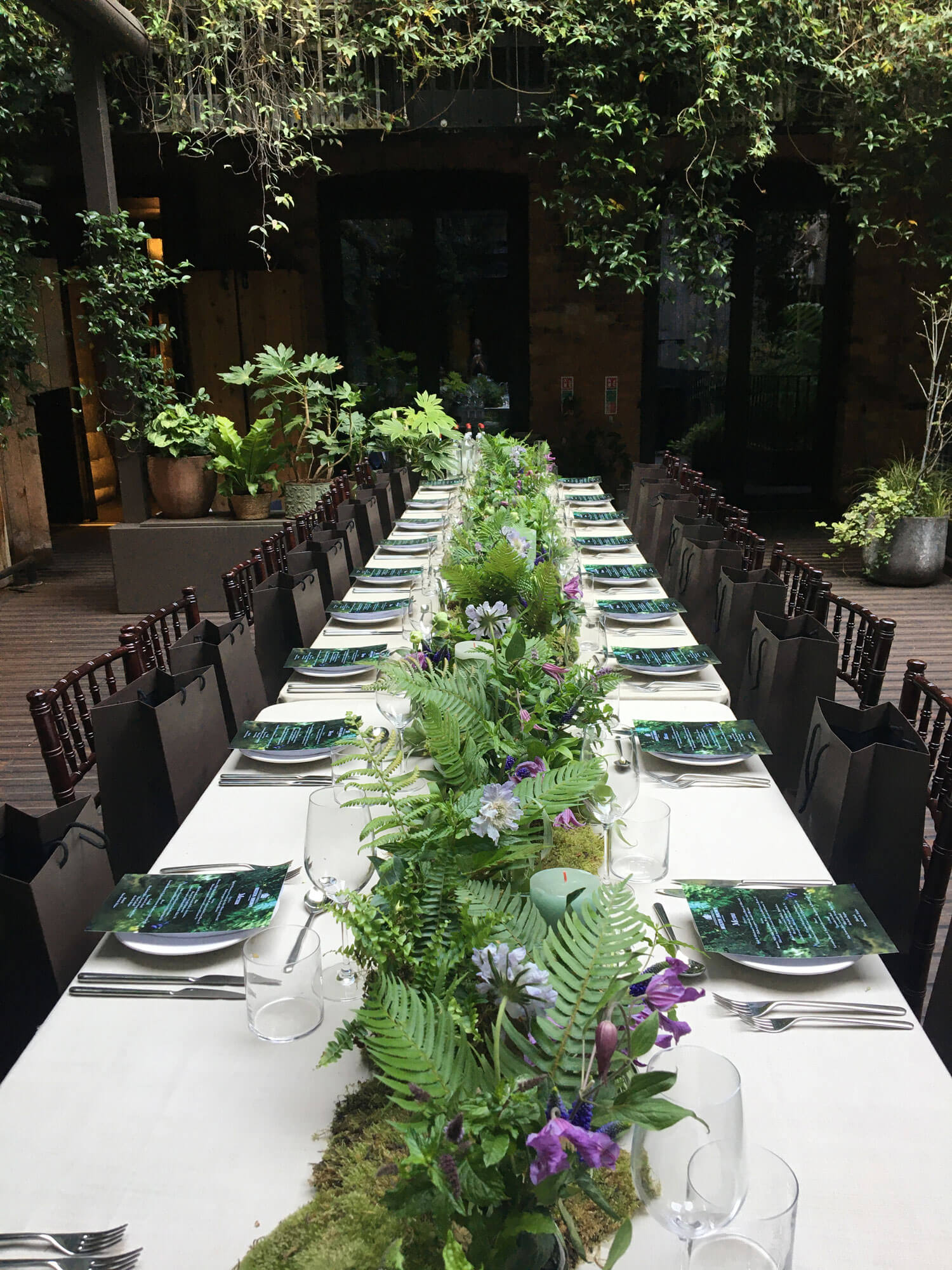 Floral tablescape for private dinner with green and purple plants and flowers used to display products. Moss, ferns and purple flowers are included with candles
