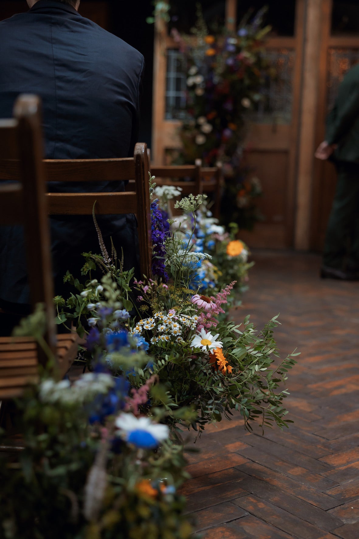 Decorative floral arrangements on a wooden floor along an aisle. Wild garden arrangements of daisies, cornflower and meadow flowers