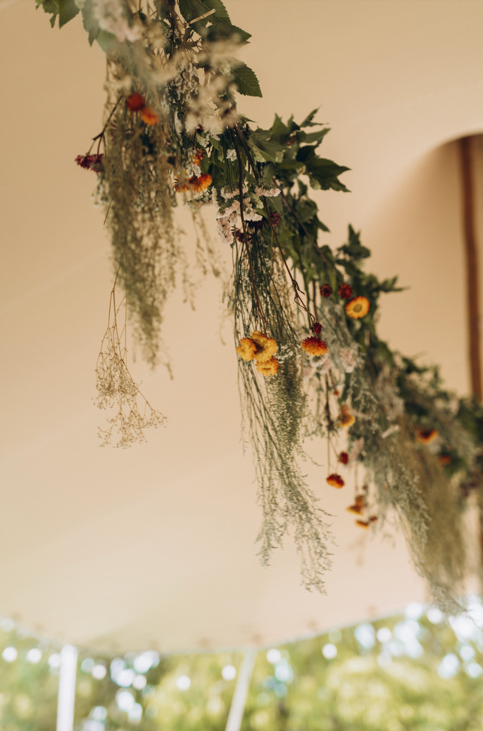 Hanging floral arrangement with greenery and small flowers against a tent canopy