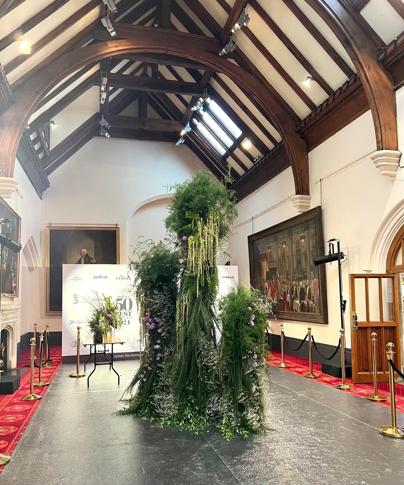 Tall and contemporary decorative floral arrangement in a room with high ceilings and paintings on the walls.