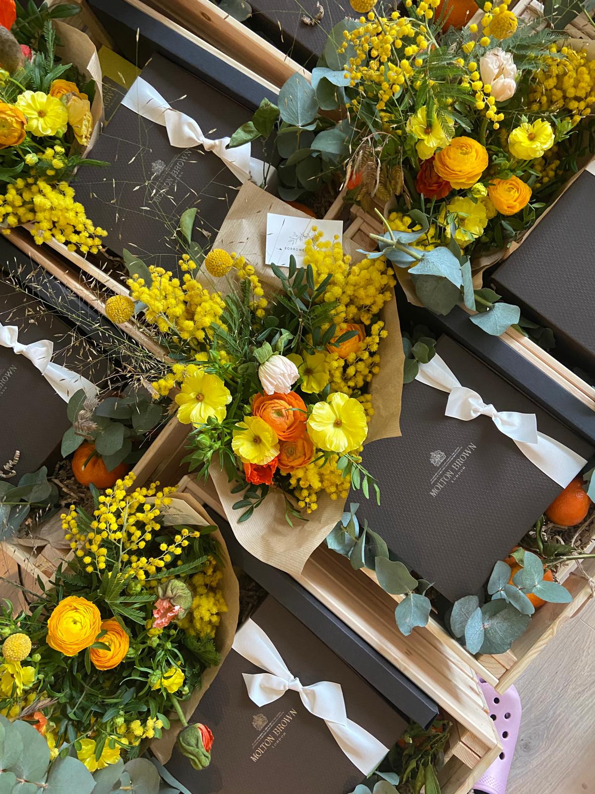 Corporate gift mail out boxes with yellow and orange spring bouquets in crates with perfume boxes and fruit