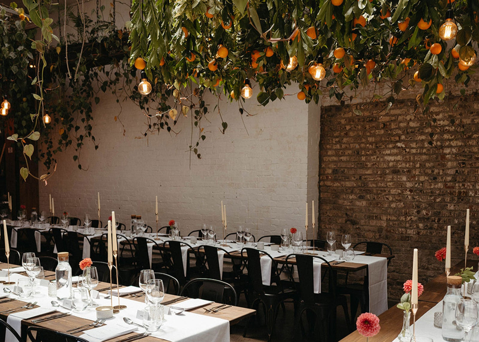 Wedding set up with suspended orange grove above tables set for dinner with vases of orange dahlia
