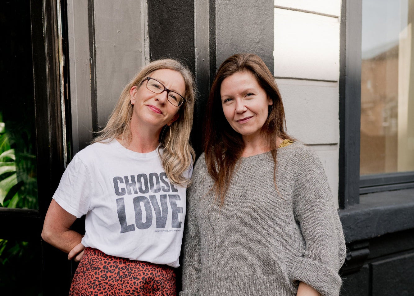 Two women standing outside a building with plants around