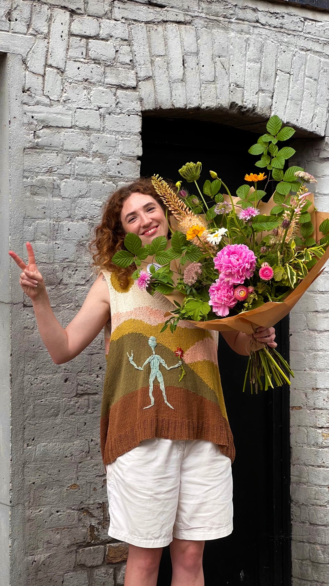 Person holding a bouquet of flowers in front of a stone wall
