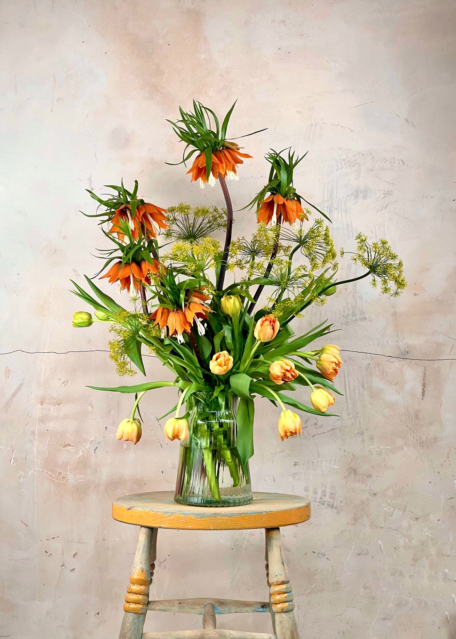 Vase of flowers on a wooden stool against a textured wall