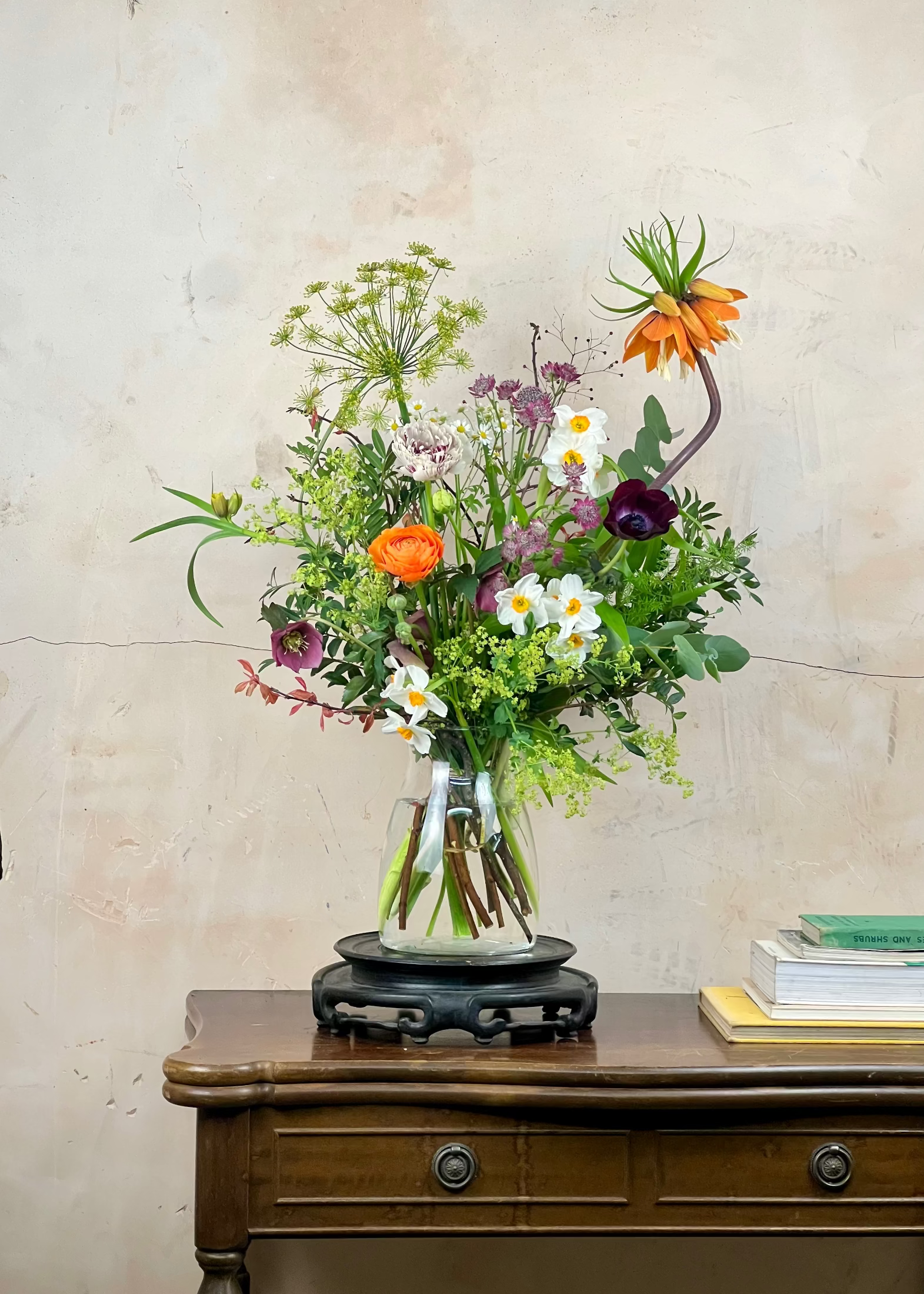 Bouquet of flowers in a glass vase on a wooden table with a light-colored wall background
