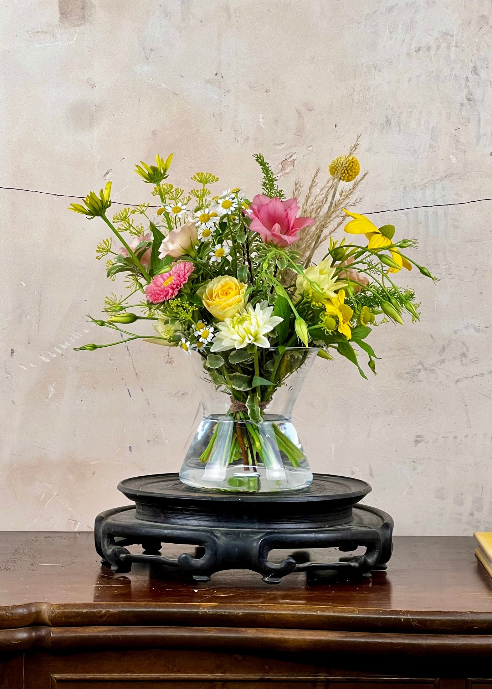 Bouquet of flowers in a clear vase on a wooden table with a textured wall background
