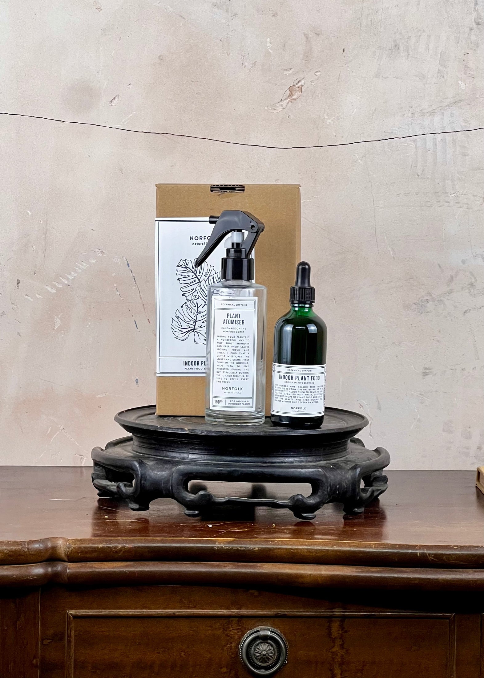 Two bottles and a box on a wooden stand against a textured wall.