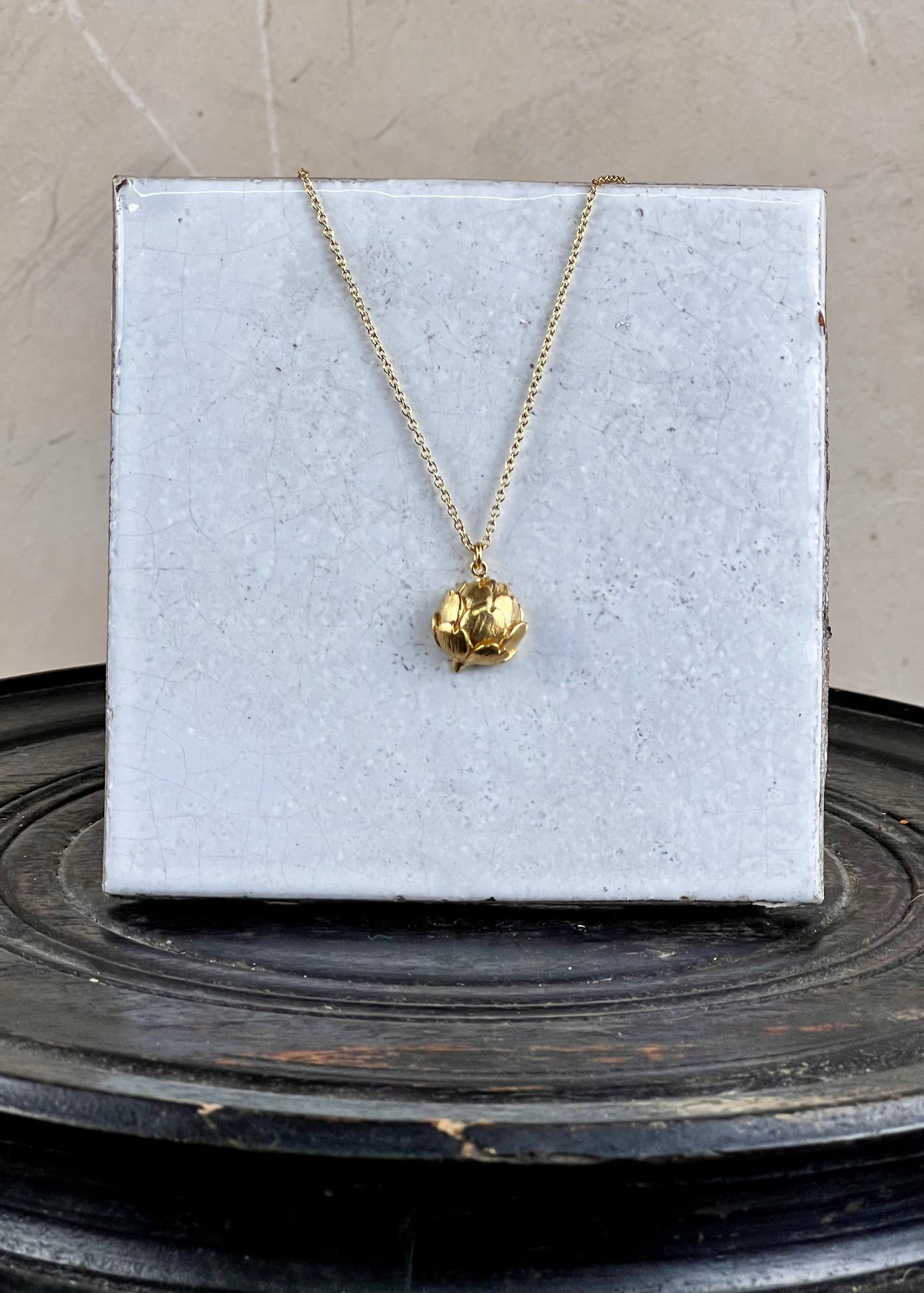 Gold necklace with a pendant on a white card against a gray background