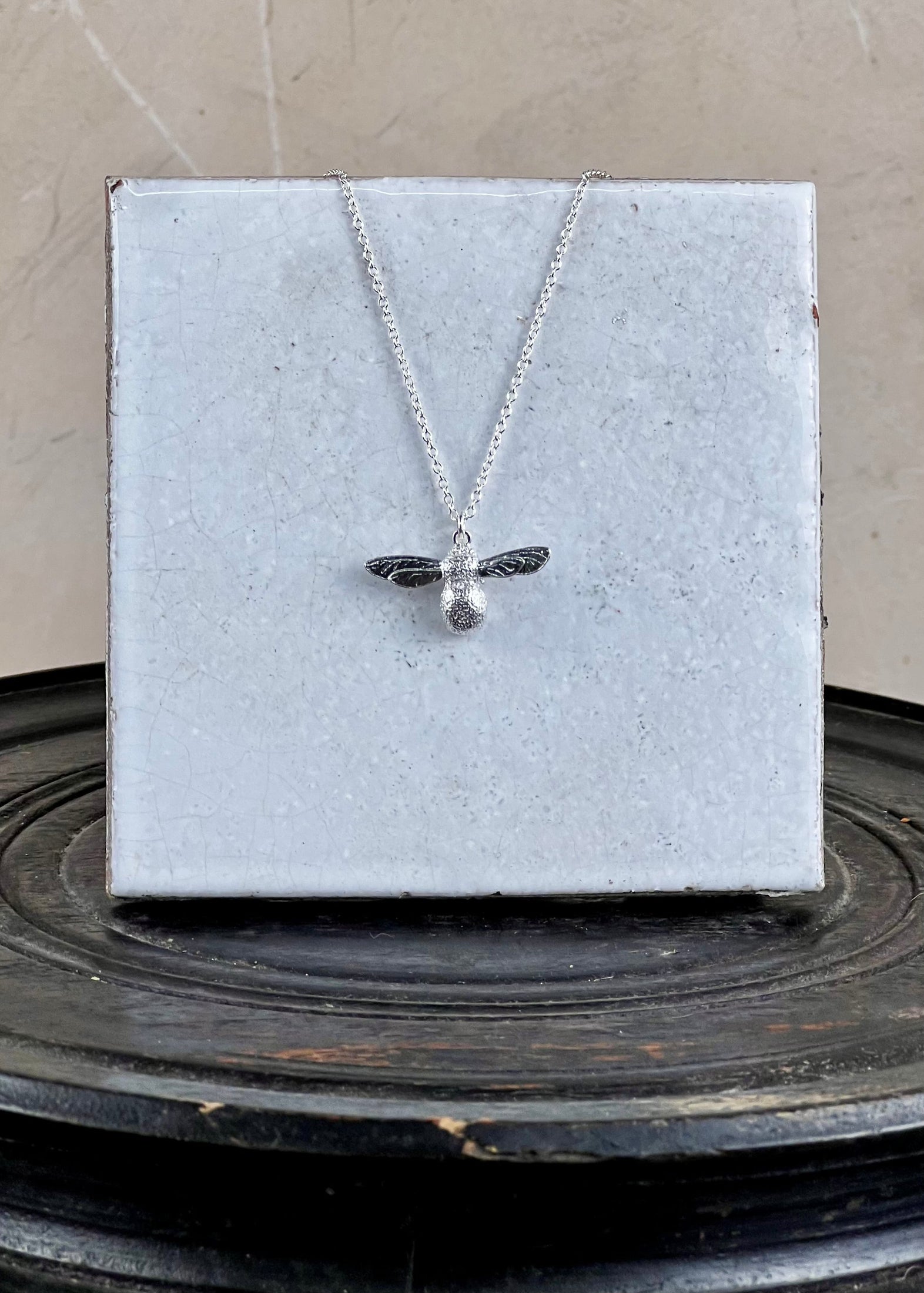 Silver bee necklace on a gray card with a textured surface