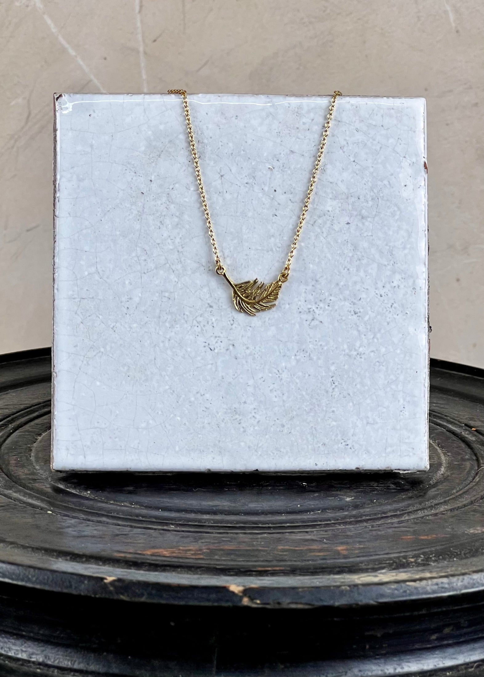 Gold necklace with a leaf pendant on a white box against a neutral background