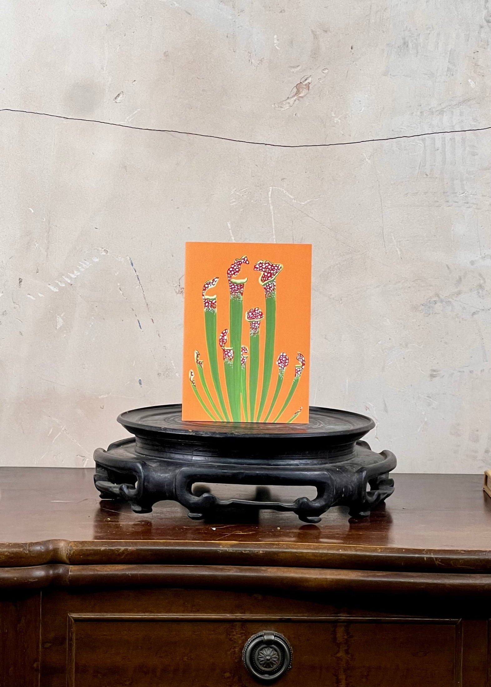 Card with floral design on an orange background on a wooden stand against a textured wall.