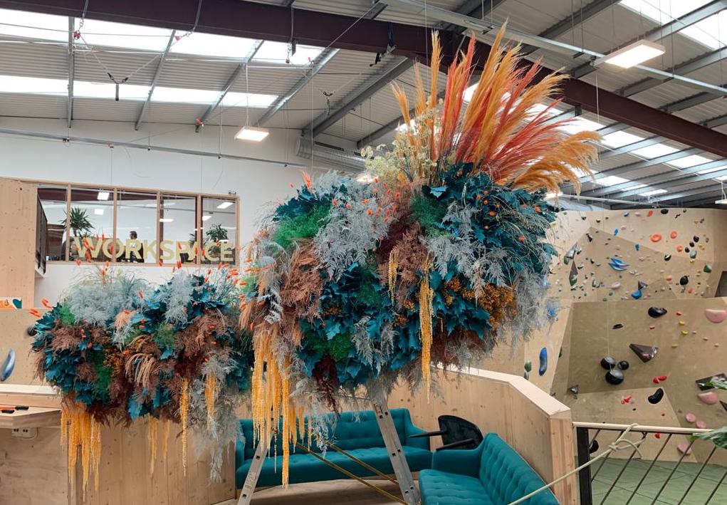Decorative dried floral clouds in bright turquoise and orange flowers hanging in a modern indoor setting of a climbing centre. Colours match company branding and background decor