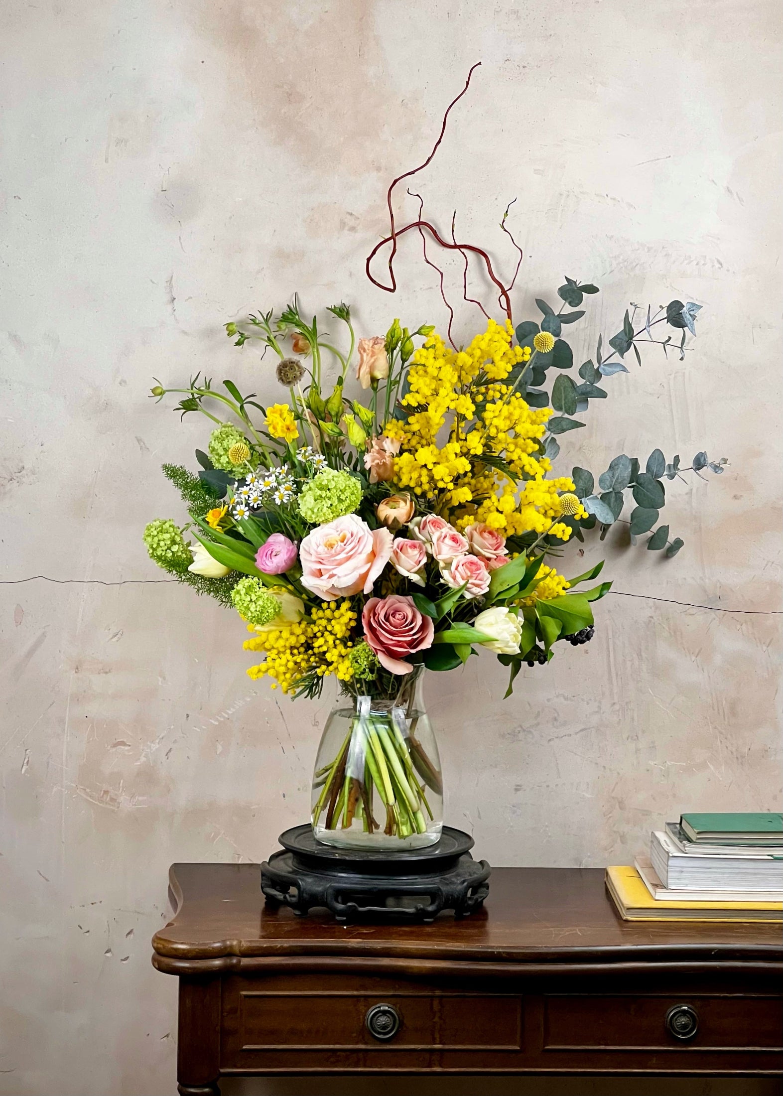Bouquet of flowers in a glass vase on a wooden table with a textured wall background