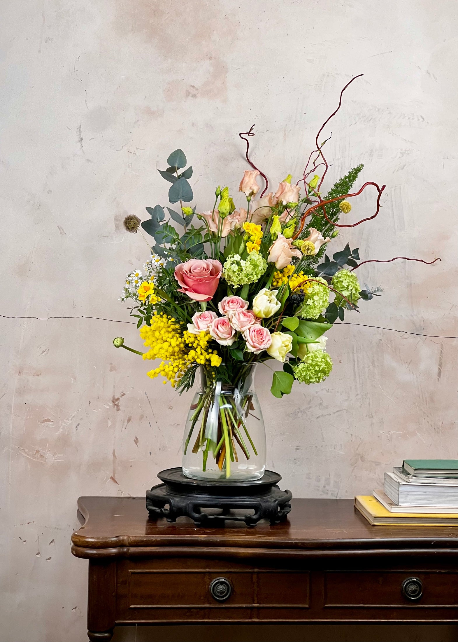 Bouquet of flowers in a clear vase on a wooden table with a textured wall background