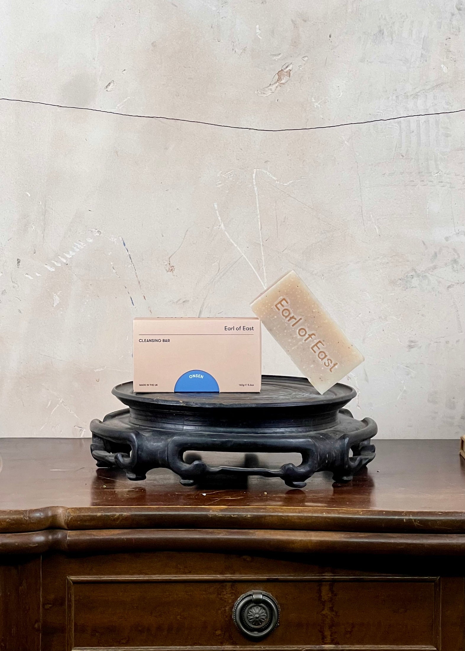 Bar of soap and packaging on a wooden stand with a textured wall background
