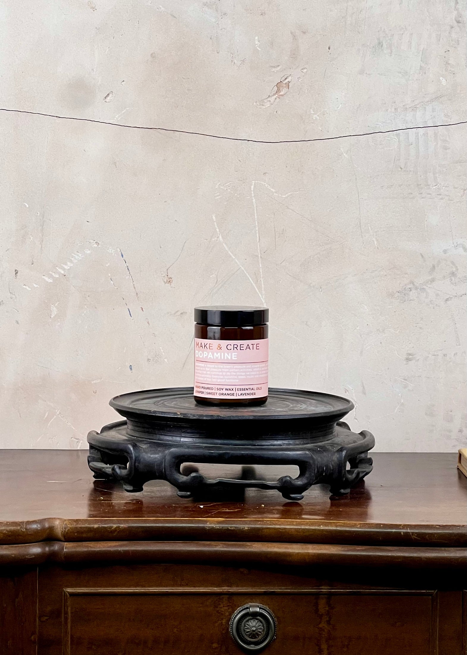 A soy wax candle jar on a wooden surface with a textured wall background