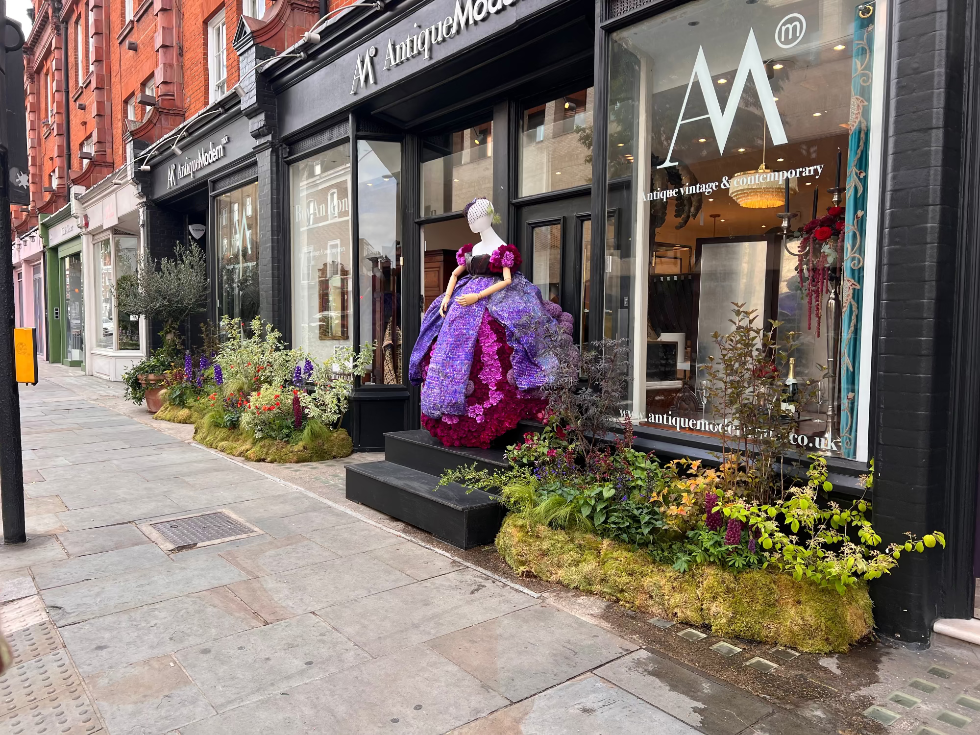 Mannequin in a purple dress made out of flowers, outside a store with decorative plants on a city street. For Chelsea in Bloom competition