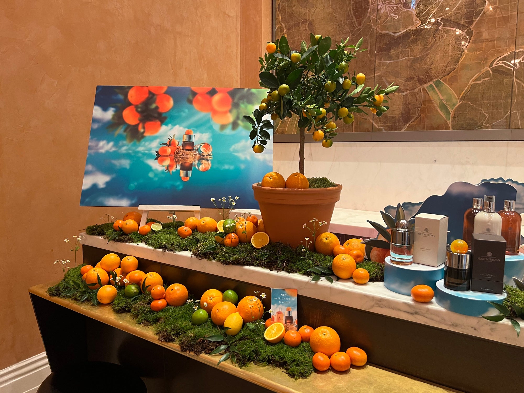 Decorative bar setup with  citrus fruits, plants, and perfume bottles on a table against a wall with a painting.
