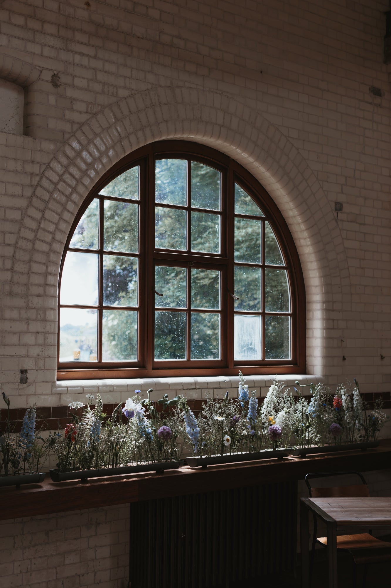 Arched window with floral decorations in a room with glazed brick walls. A floral meadow is under the window and captures the light coming through the window