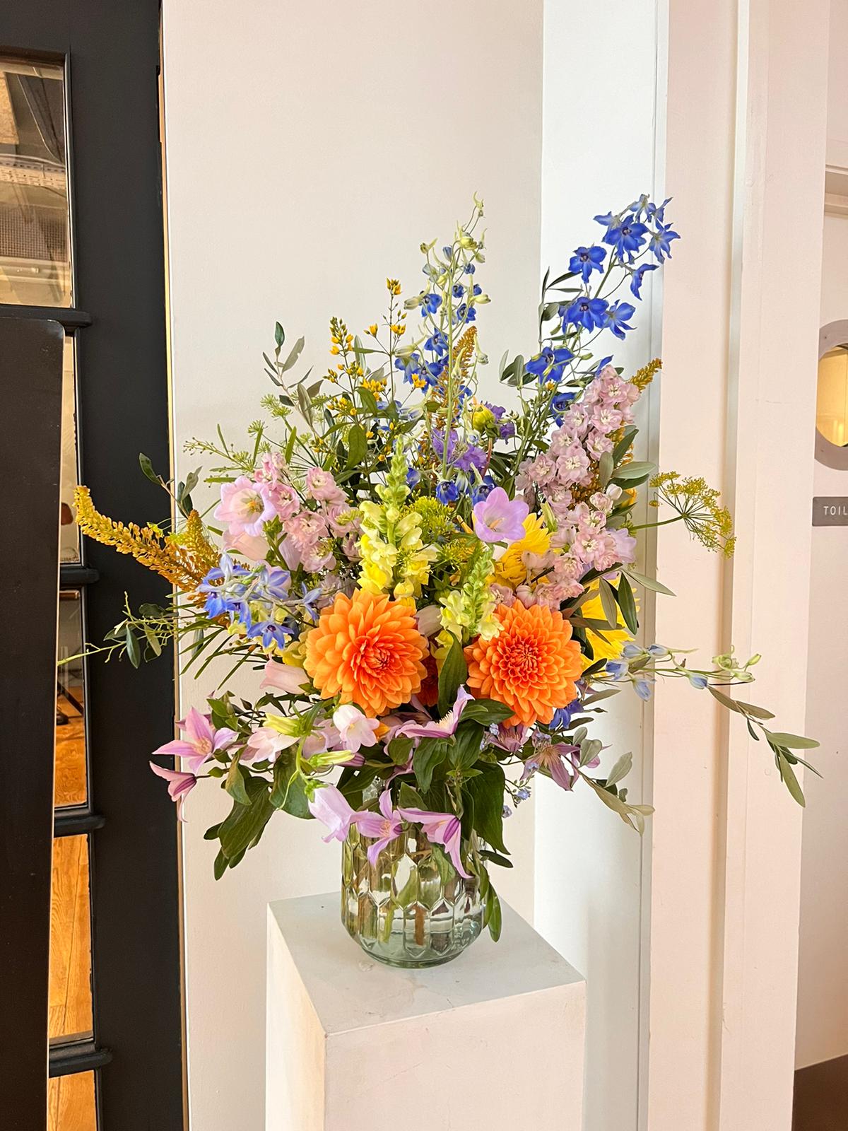 Bouquet of colourful pastel flowers in a clear vase on a white plinth in contemporary restaurant.