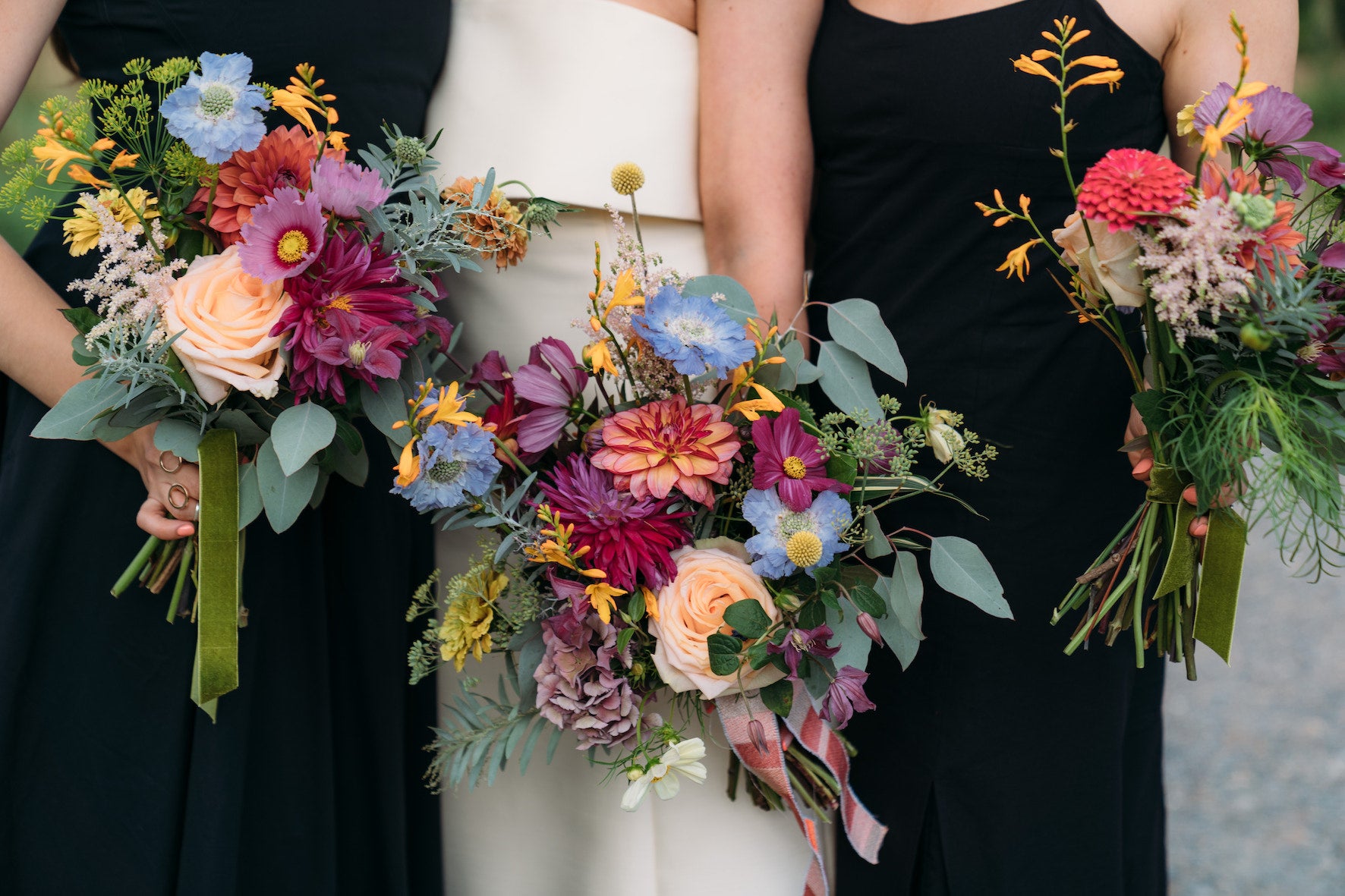 Three women in black dresses holding colourful flower bouquets. late summer bouquets of roses, dahlia, scabious, cosmos and craspedia
