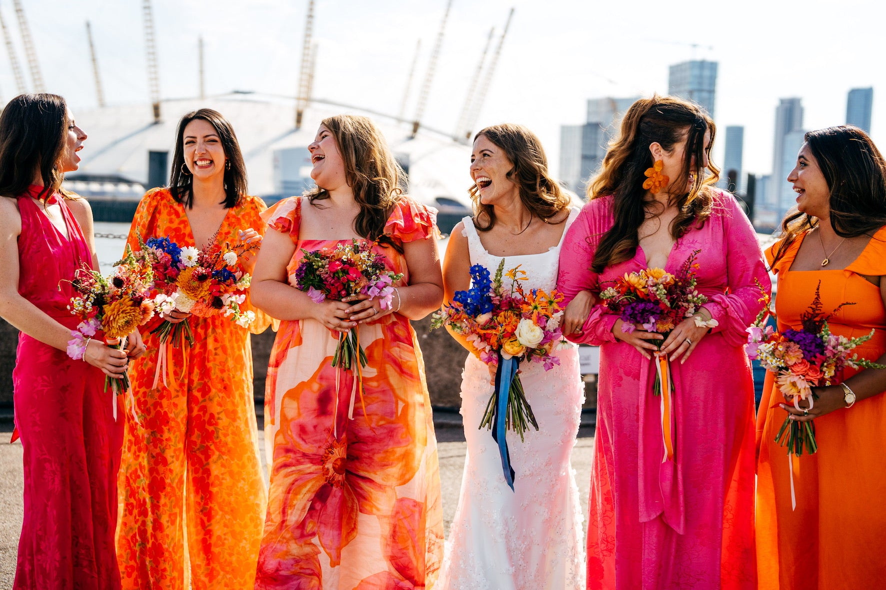 bride and 5 bridesmaids in colourful dresses with bright floral bouquets against a city  of London skyline. bright summer flowers in each bouquet