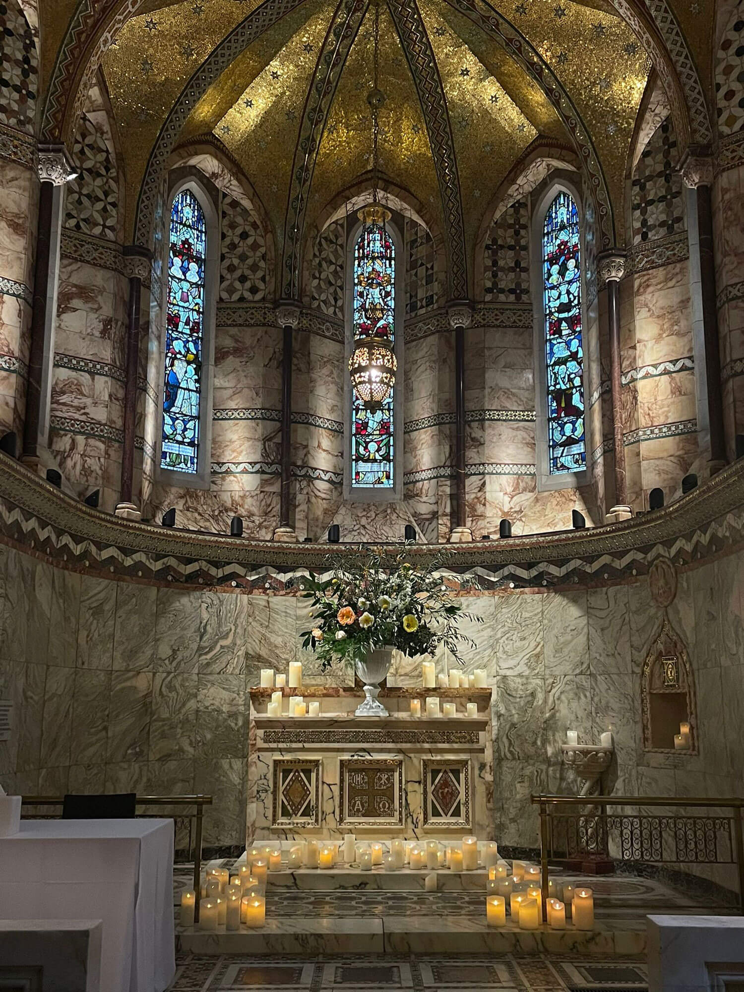 candle lit chapel with a large arrangement of flowers in a white urn at the altar