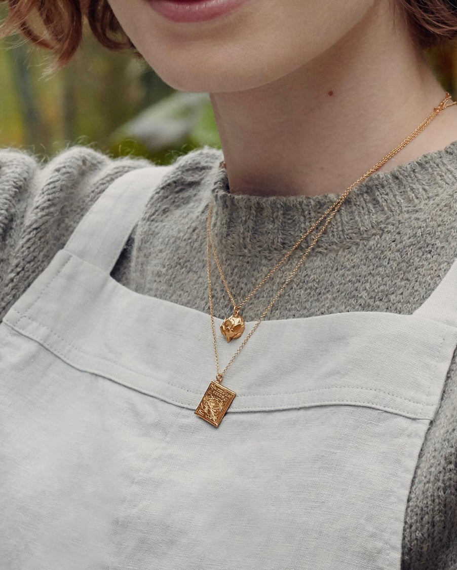 Person wearing a gold necklace with a pendant, blurred background