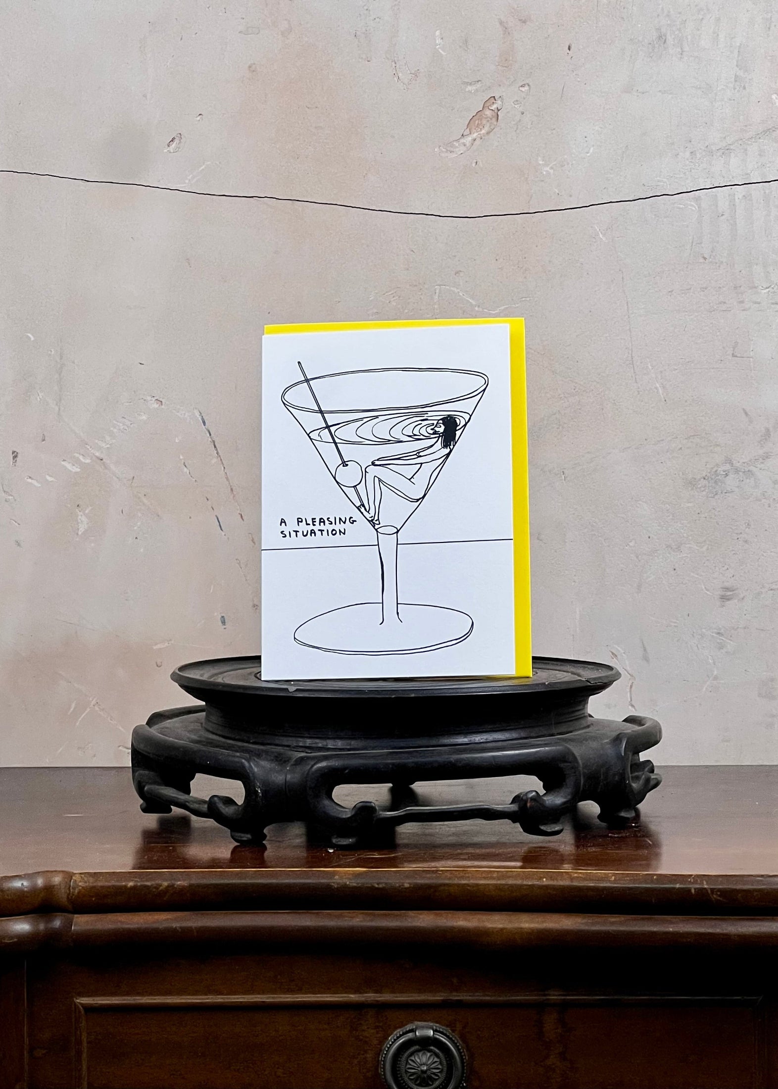 Card with a martini glass design on a wooden stand against a textured wall.