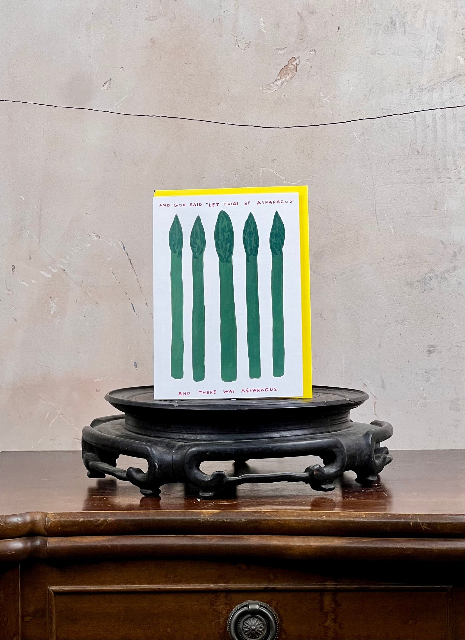Card with green asparagus illustration on a wooden stand against a textured wall.