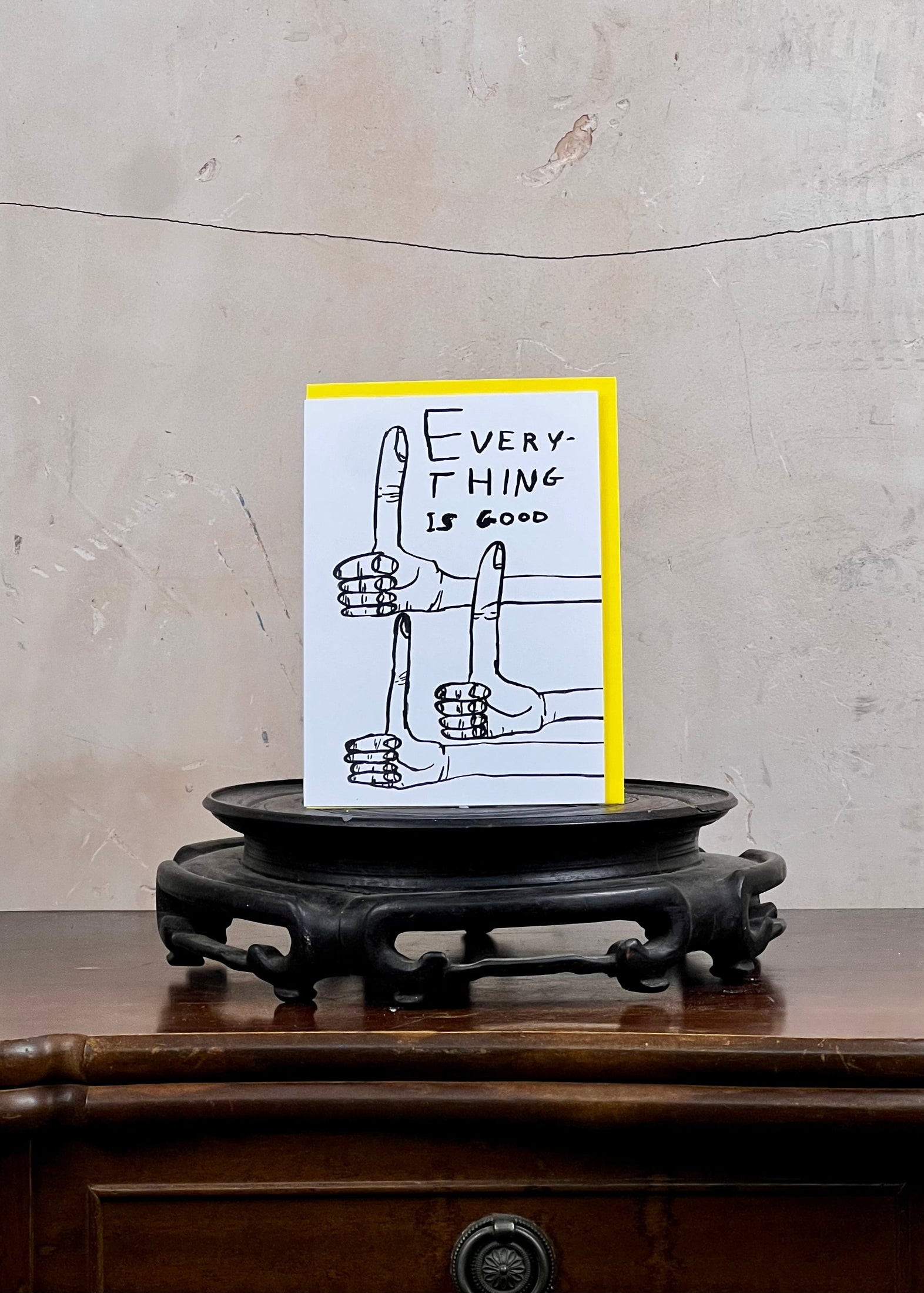 Card with a hand gesture illustration and 'Everything is Good' text on a wooden stand against a textured wall.