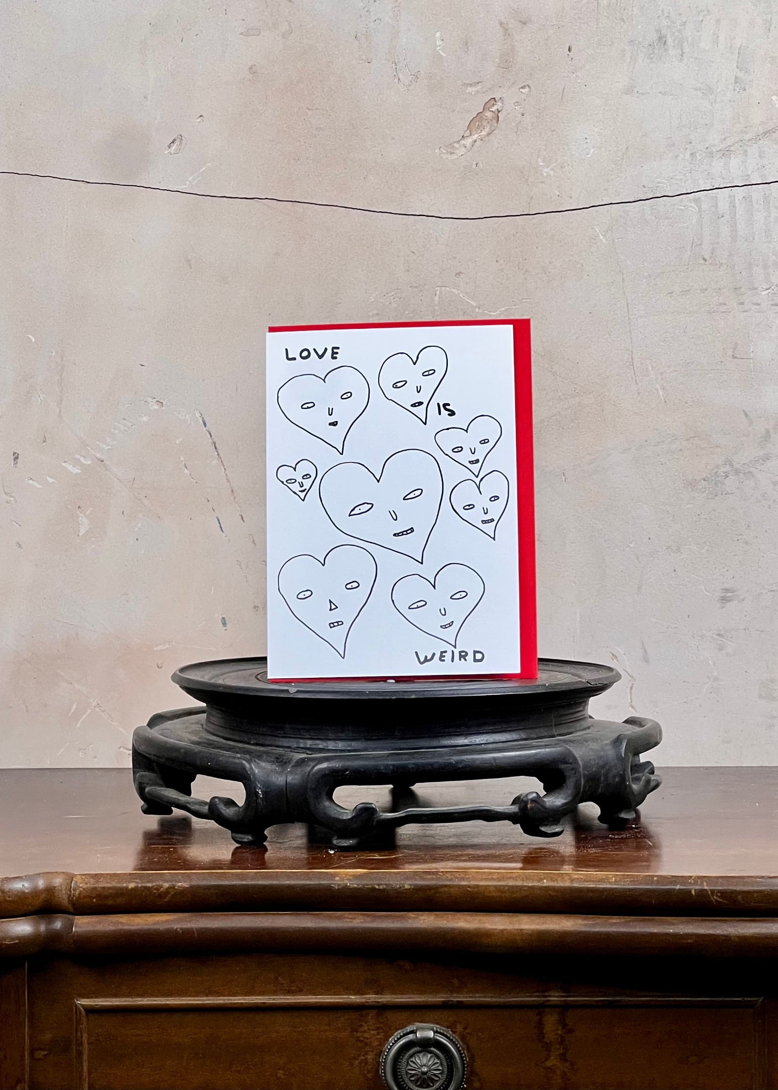 Card with heart designs and text on a stand against a textured wall.