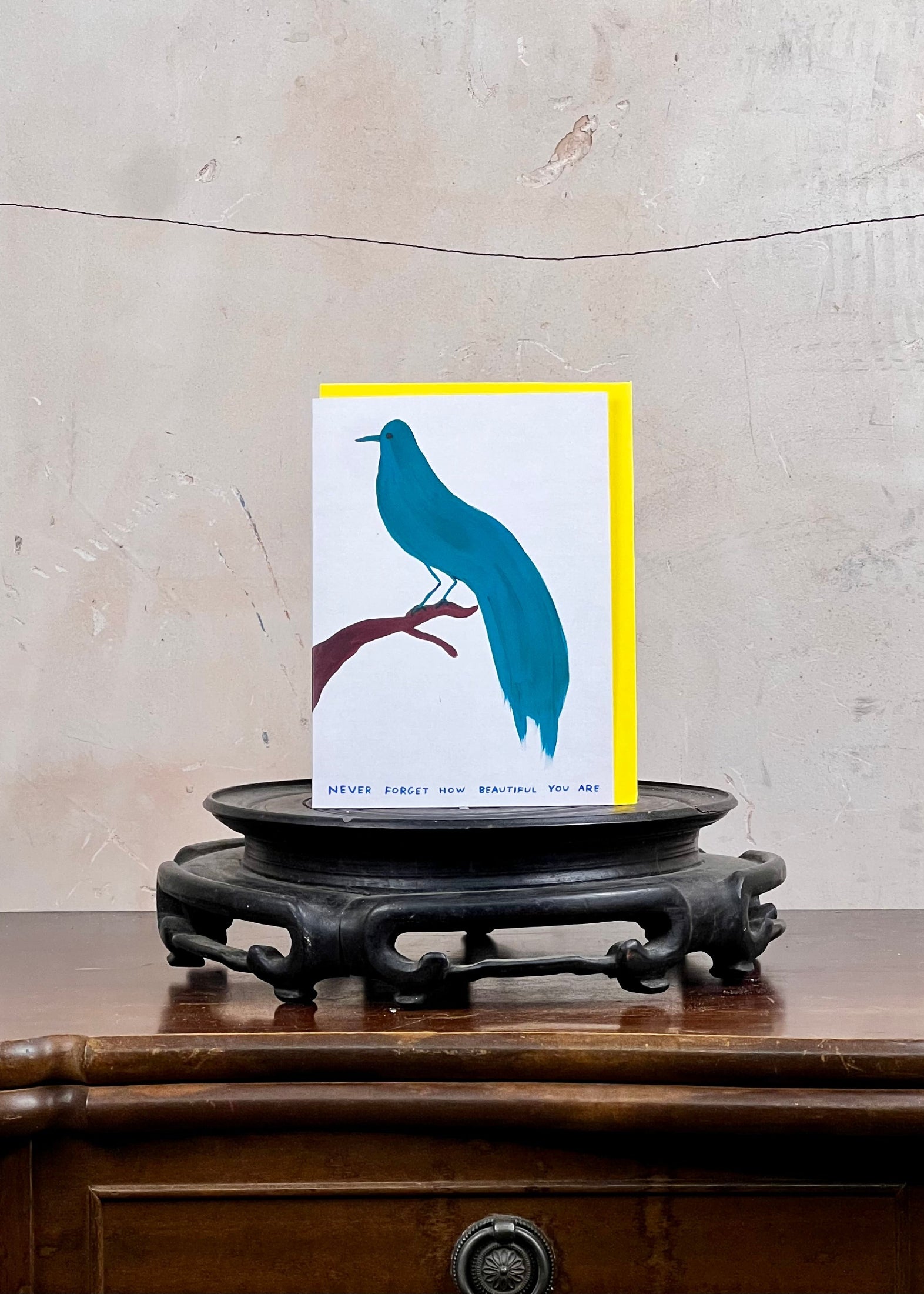 Card with blue bird design on a wooden stand against a textured wall.