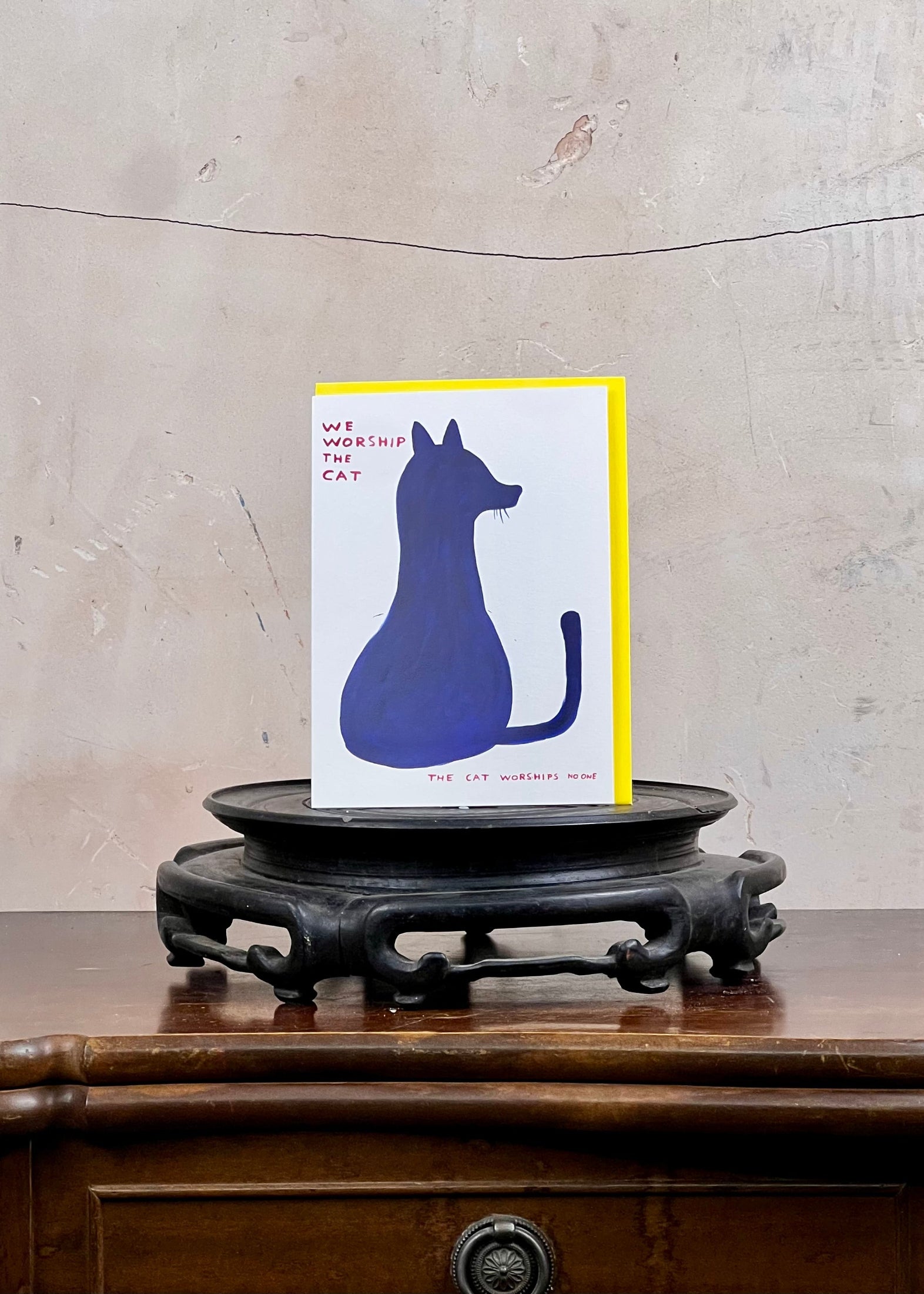 Card with blue cat illustration on a wooden stand against a textured wall.