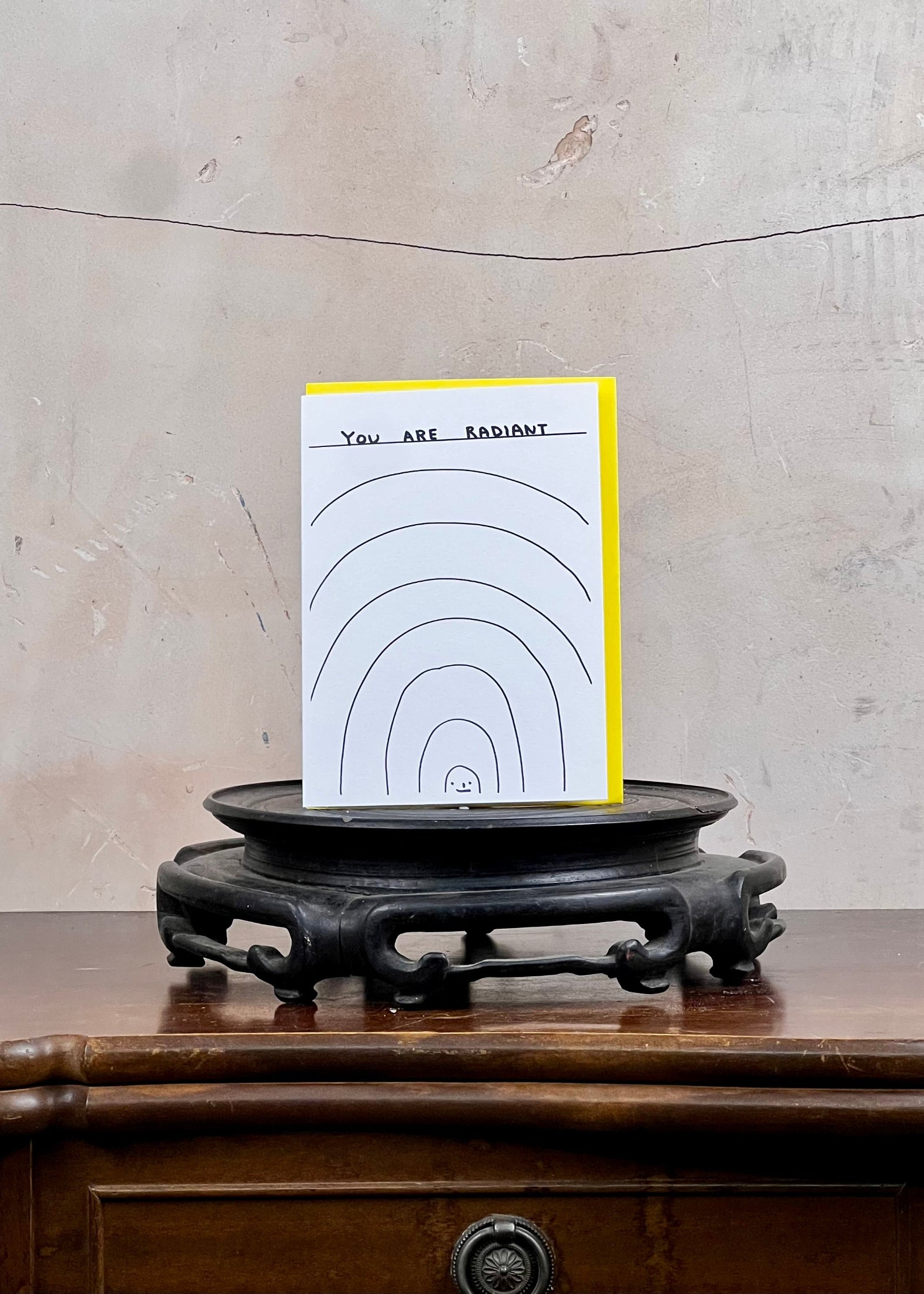 Card with 'You are radiant' text on a wooden stand against a textured wall.