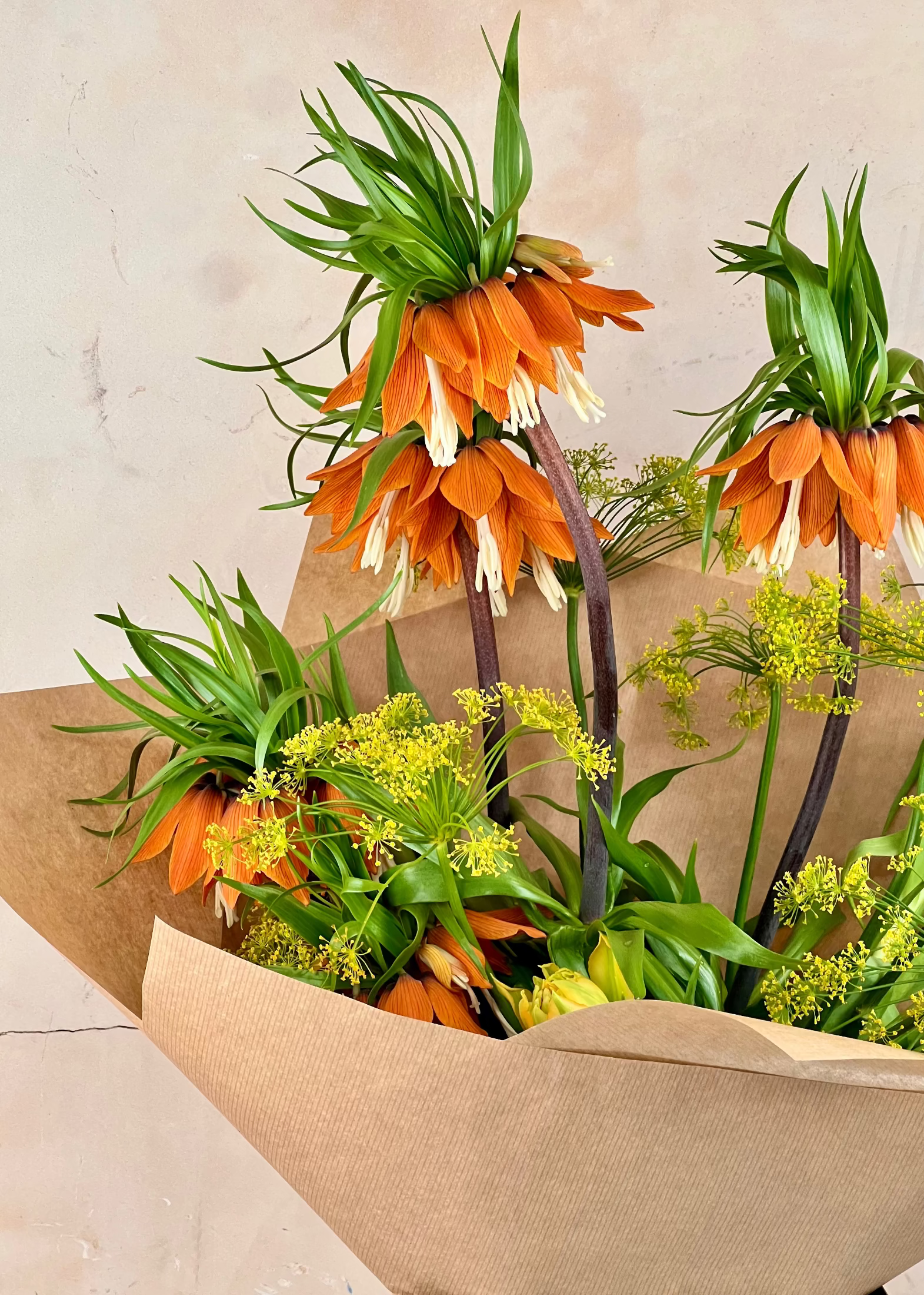Bouquet of orange and green flowers wrapped in brown paper against a neutral background