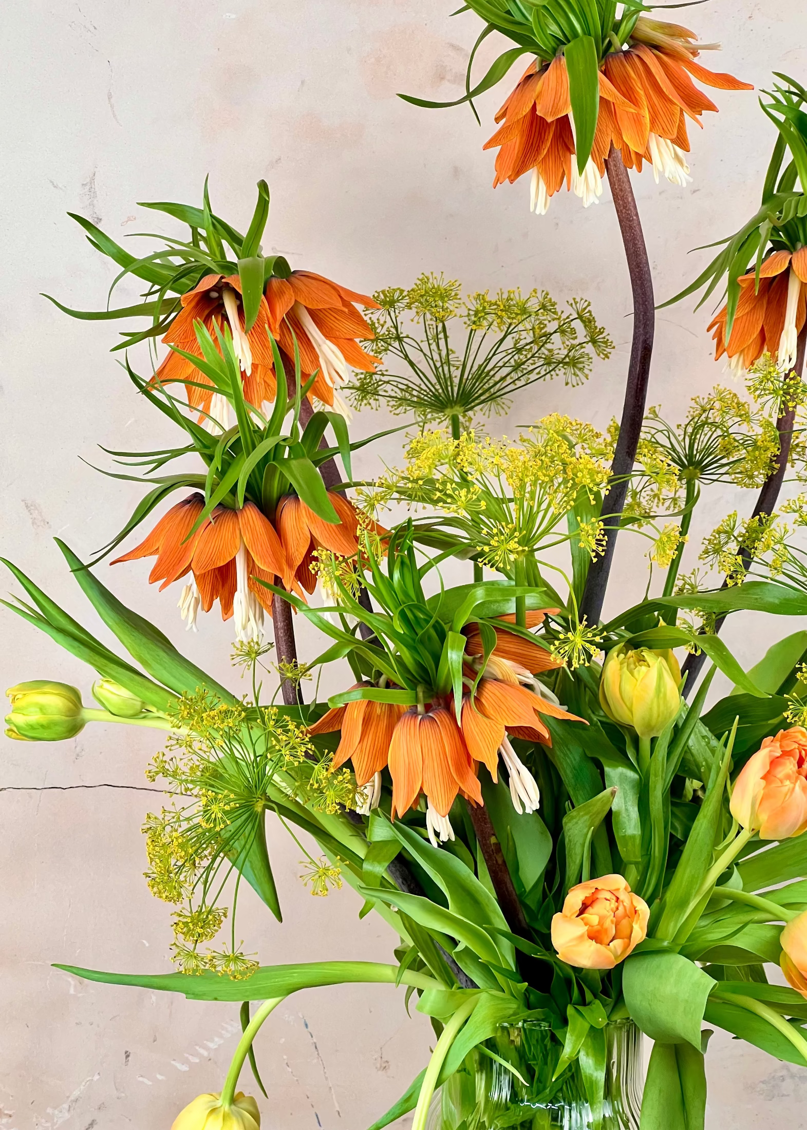 Bouquet of orange and green flowers in a clear vase against a light background