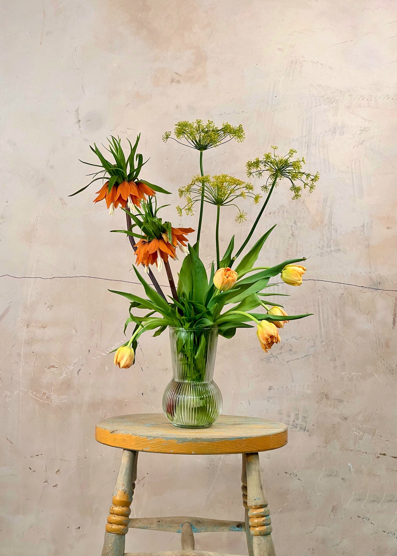 Vase with flowers on a wooden stool against a textured wall