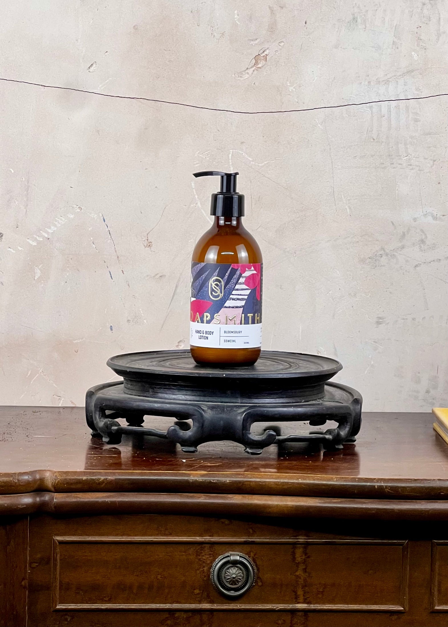 Hand and body lotion in a brown bottle with a colorful label on a wooden surface with a textured wall background