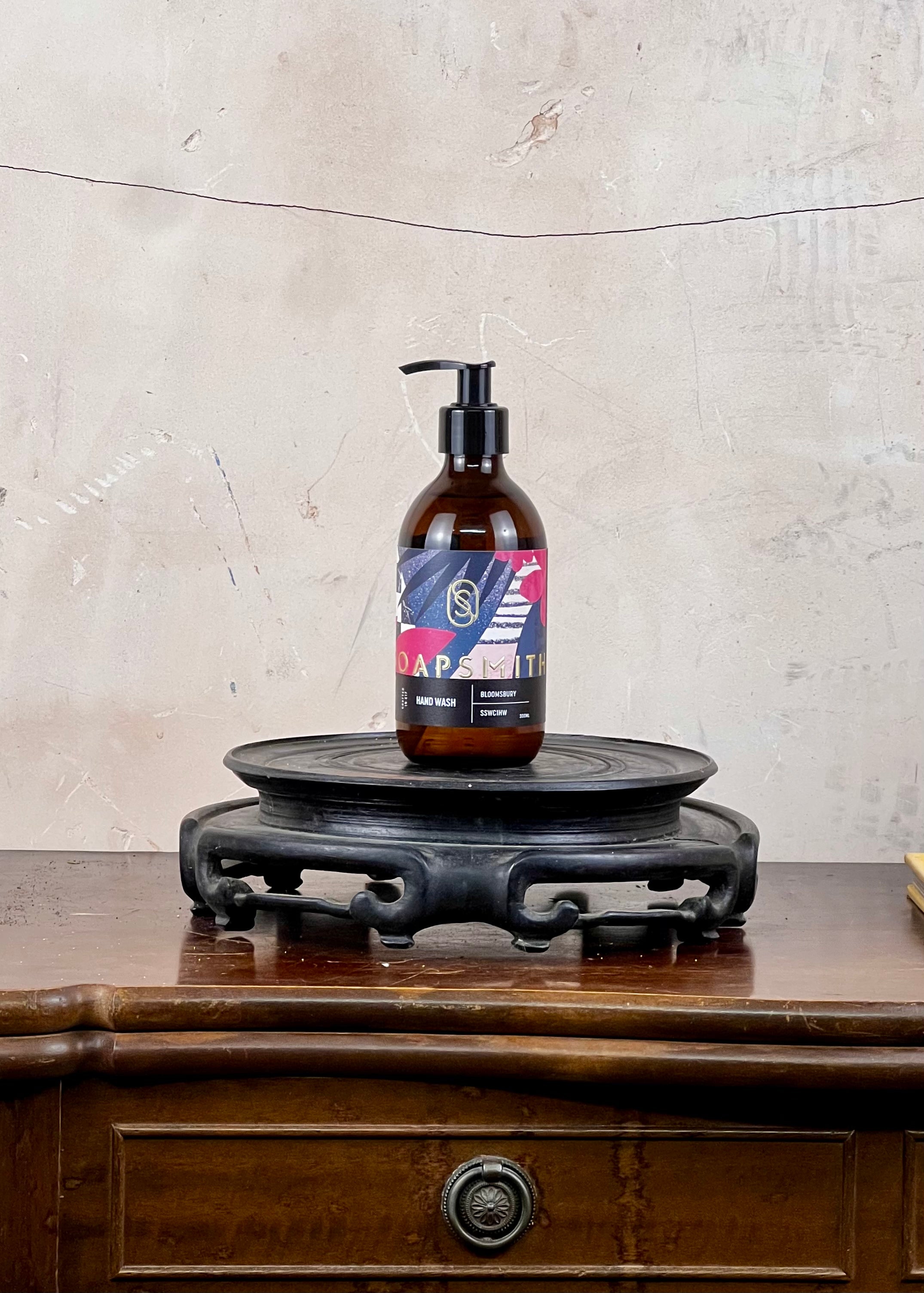 Hand wash in a brown glass bottle with a colorful label on a wooden surface and stone wall background