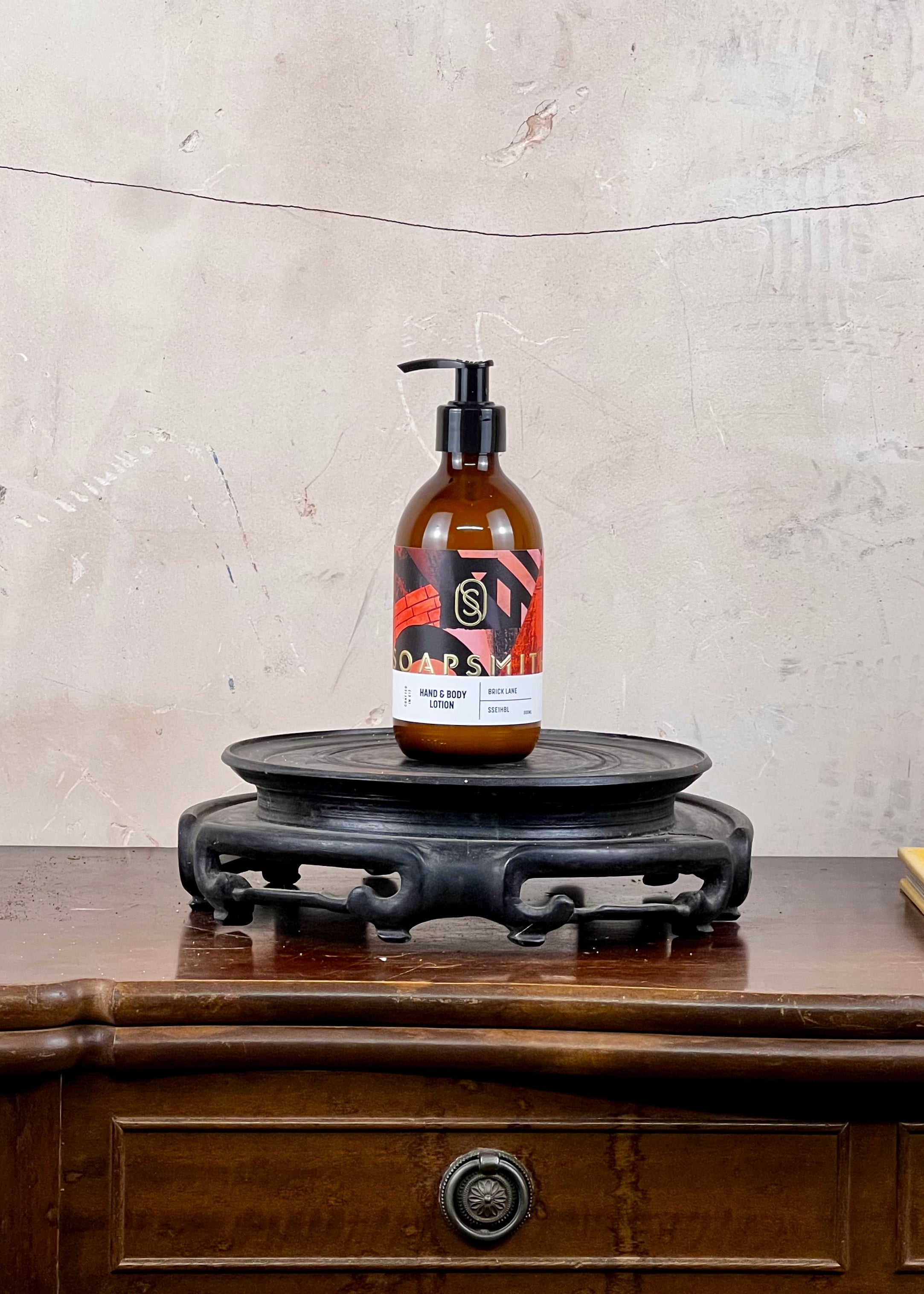 Hand and body lotion in a brown bottle with a colorful label on a wooden surface with a textured wall background