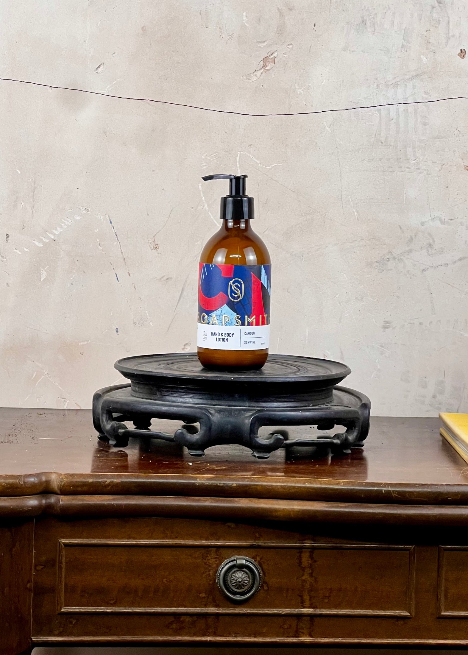 Hand and body lotion in a brown bottle with a colorful label on a wooden surface with a textured wall background