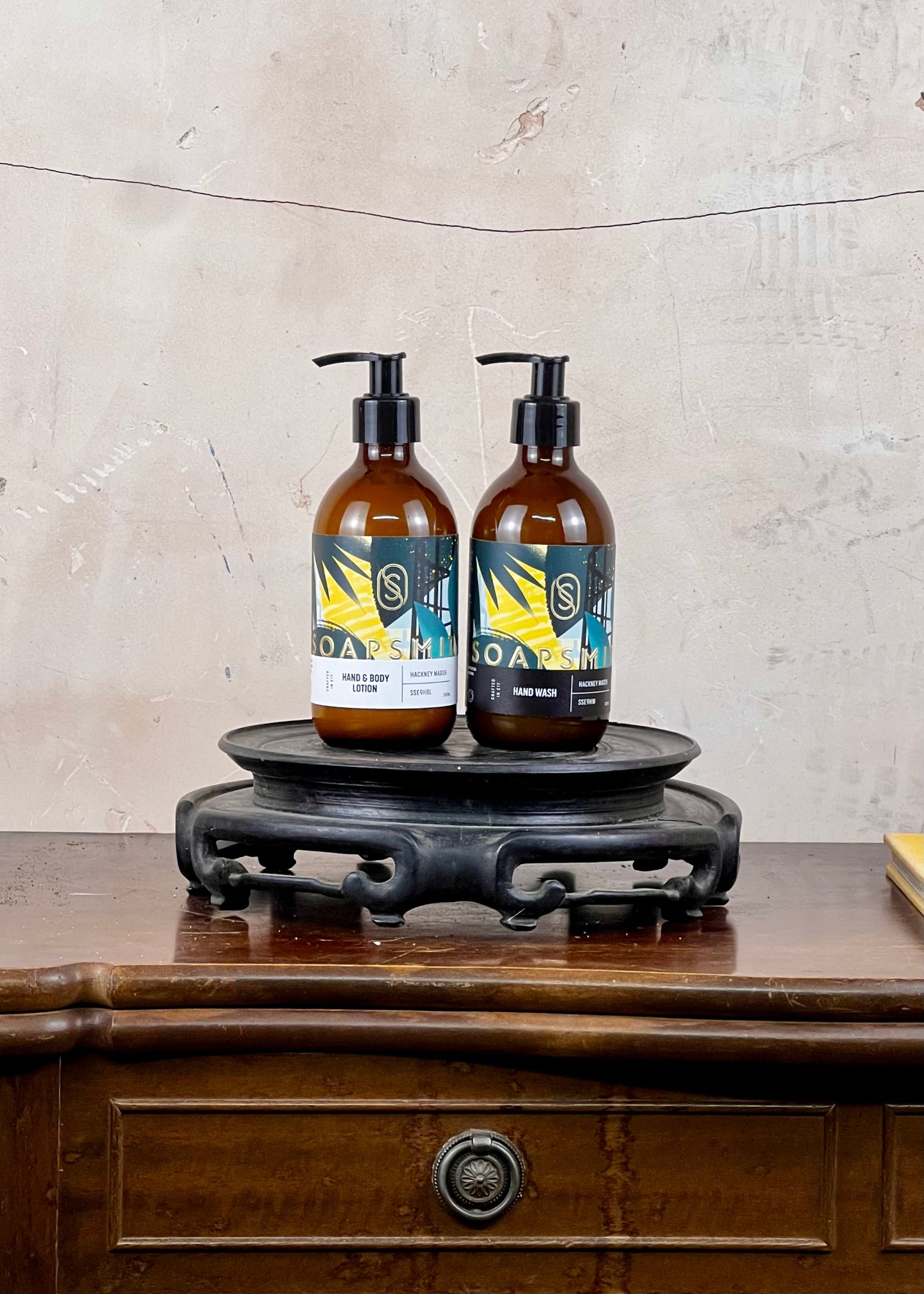 Two bottles with pump dispensers on a wooden stand against a textured wall.