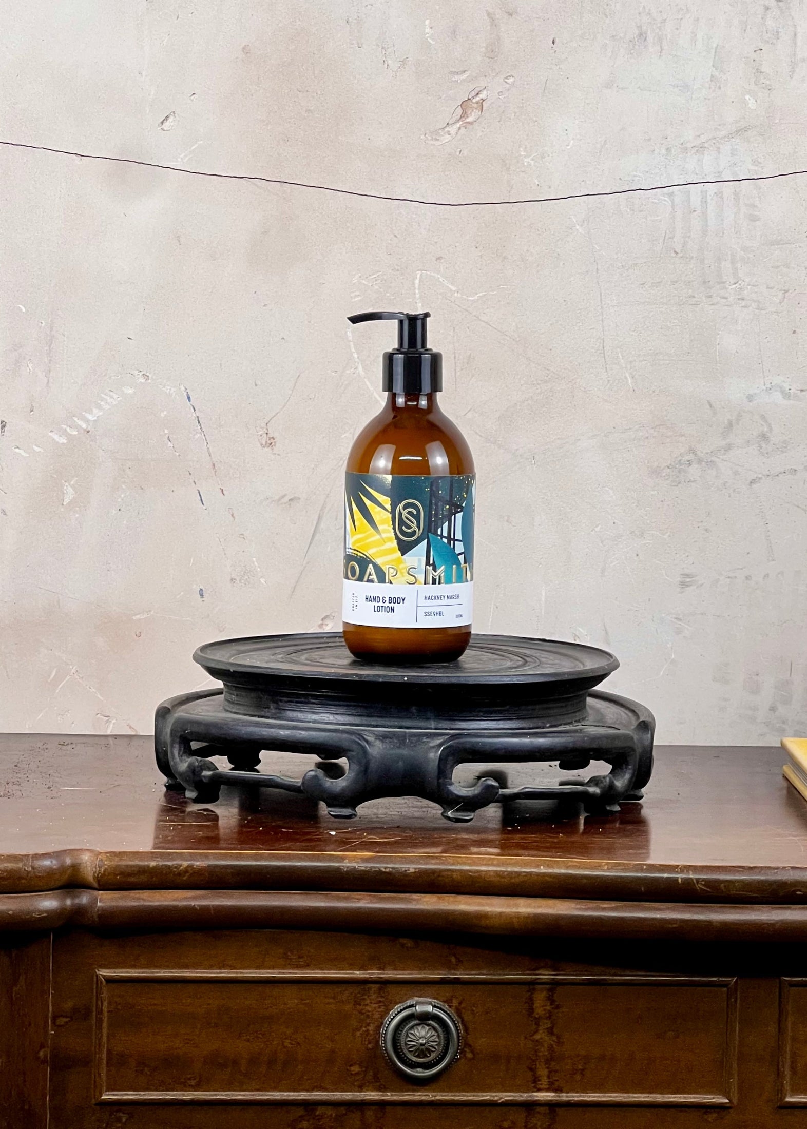 Hand and body lotion in a brown bottle with a colorful label on a wooden surface with a textured wall background