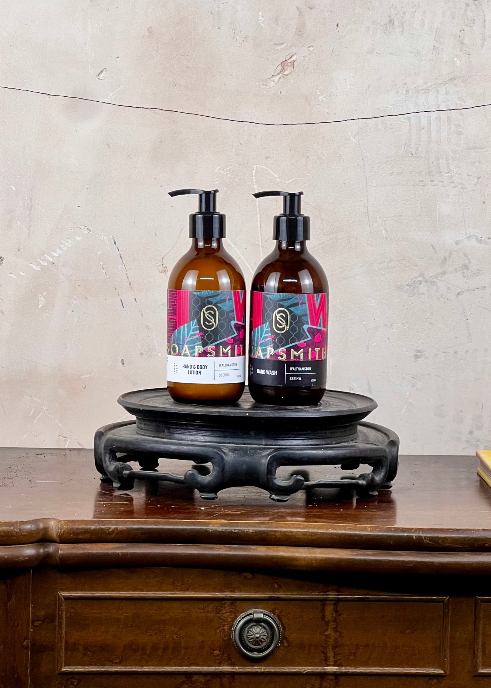 Two bottles of soap on a wooden stand with a textured wall background