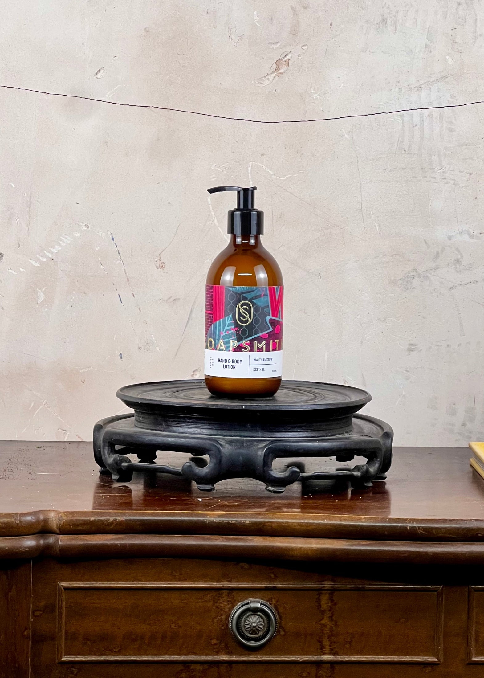 Hand and body lotion in a brown bottle with a colorful label on a wooden surface with a textured wall background