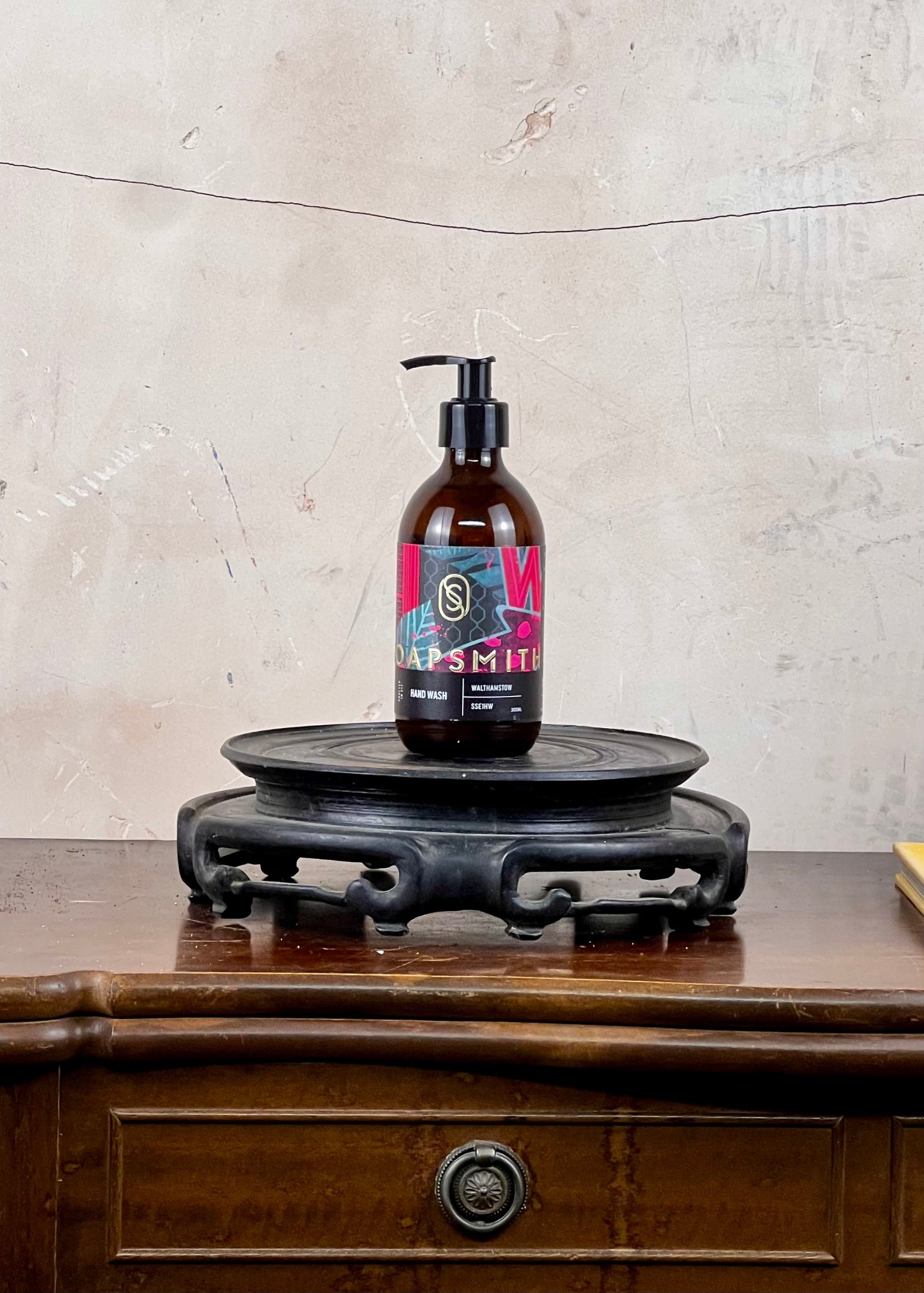 Hand wash in a brown glass bottle with a colorful label on a wooden surface and stone wall background